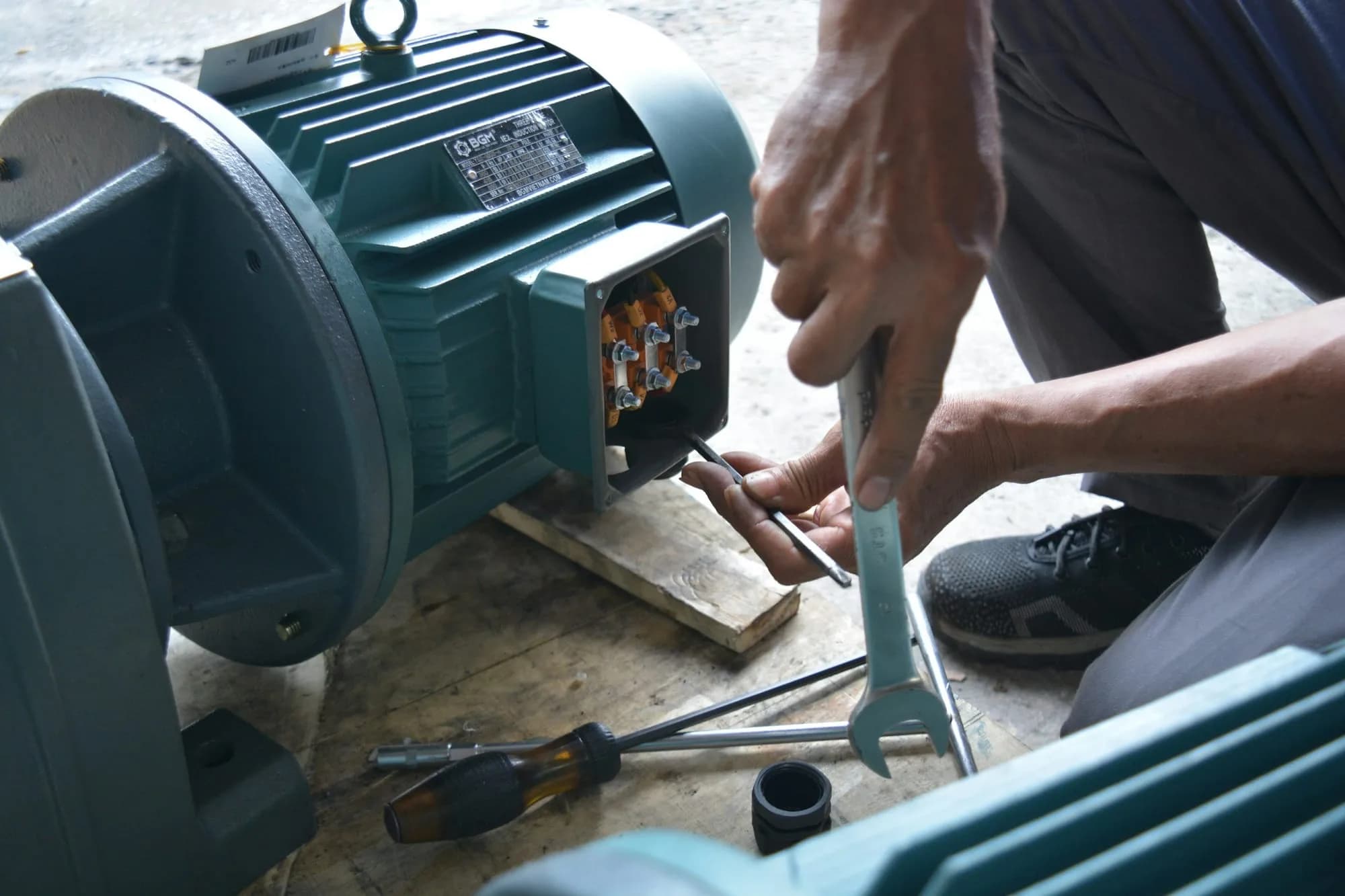 Técnico apretando con llave los bornes de un motor eléctrico industrial durante una mantención