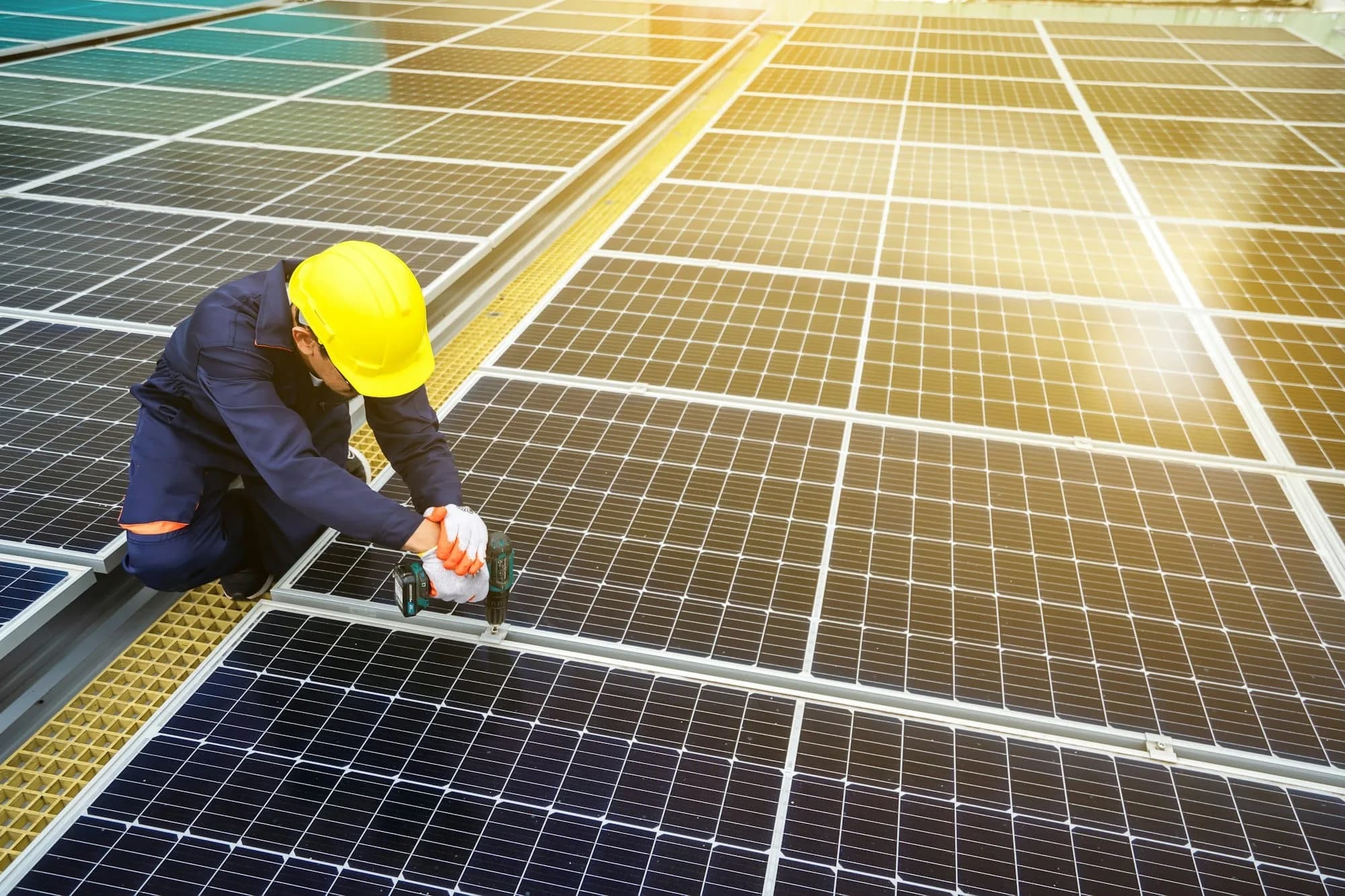 Trabajador con casco amarillo fijando paneles solares sobre una techumbre, con el sol reflejado en los módulos