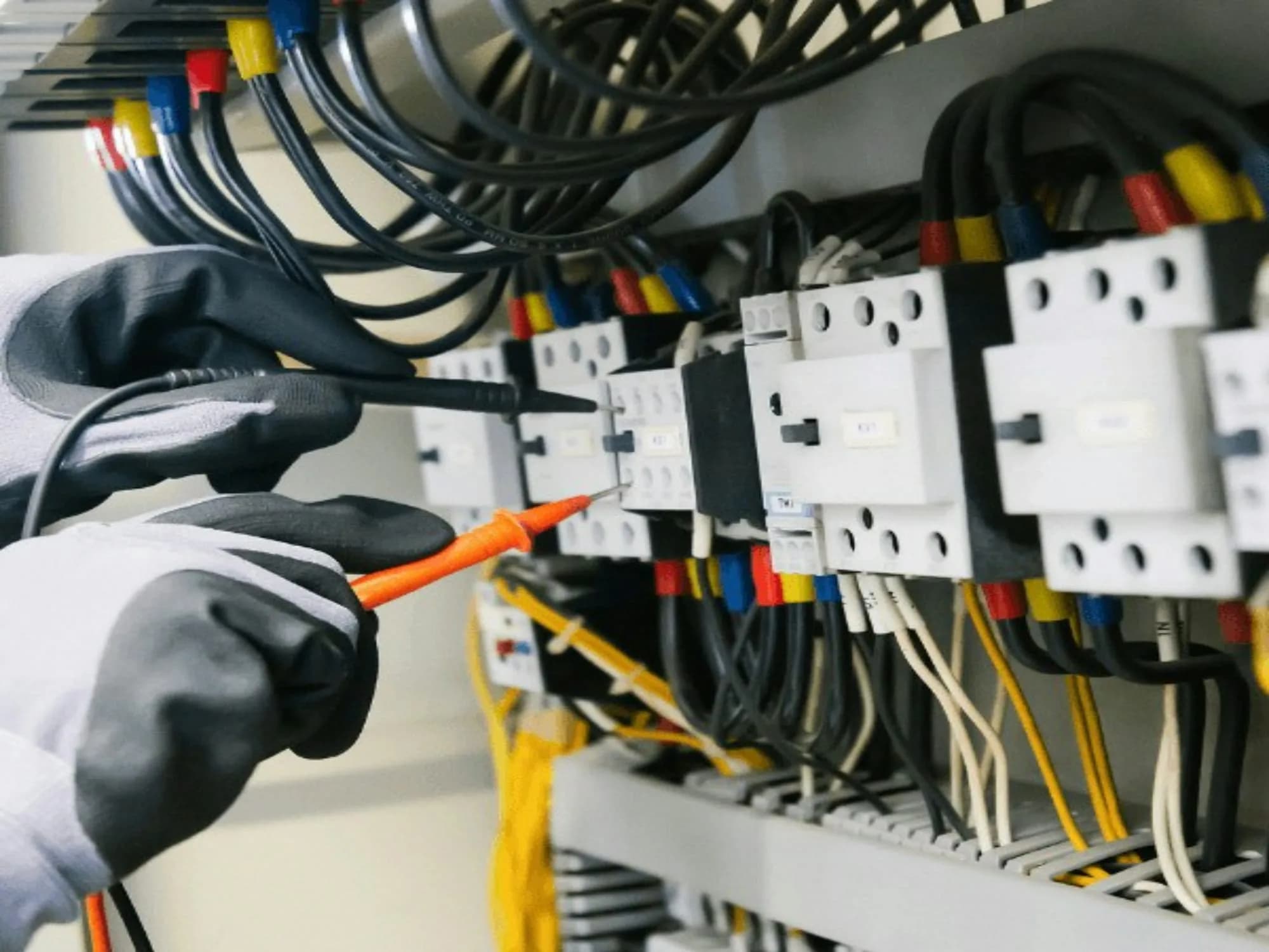 Electricista con guantes midiendo con las puntas de un multímetro los contactores de un tablero eléctrico