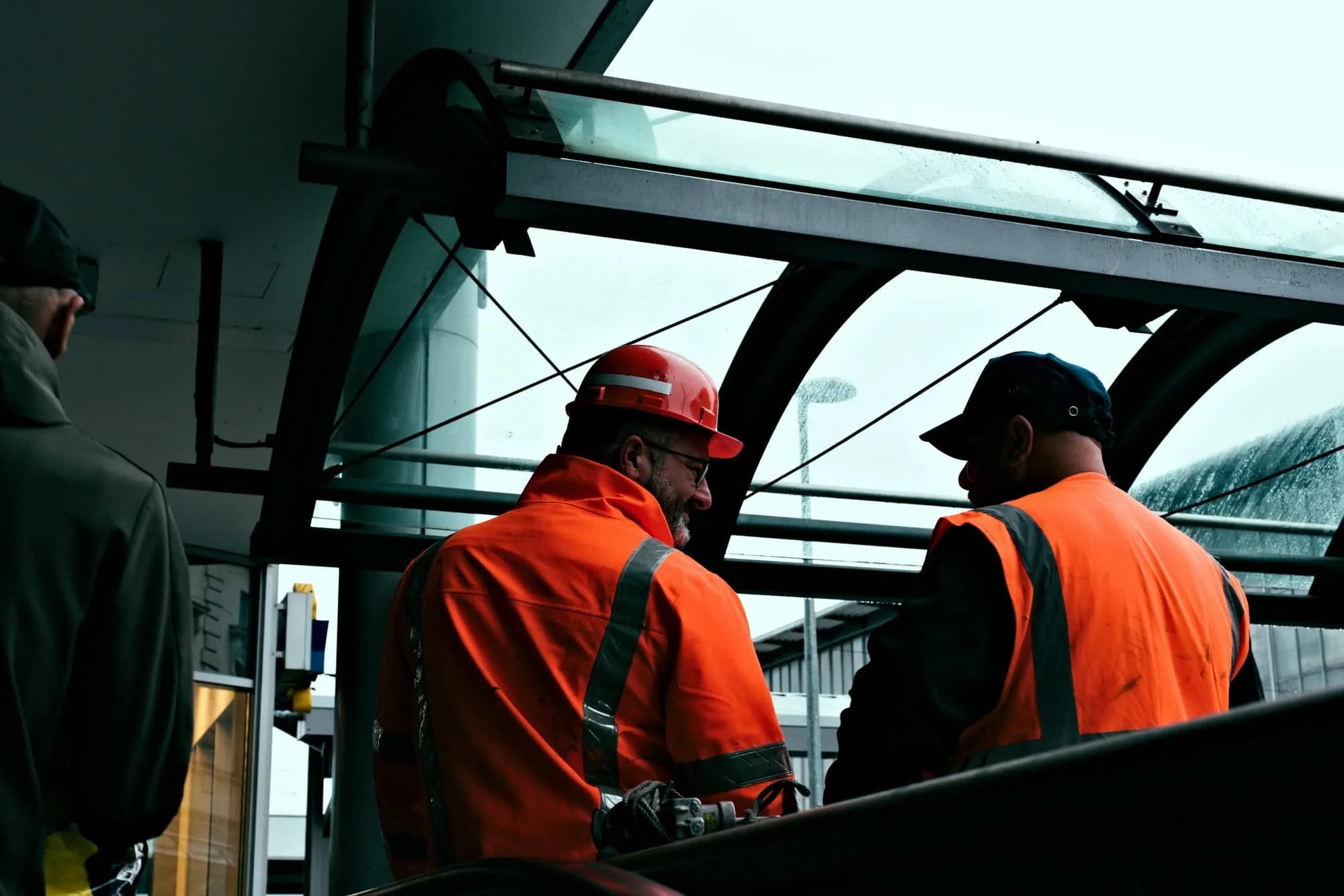 Dos trabajadores con casco y chaqueta reflectante naranja coordinando una tarea en una faena techada