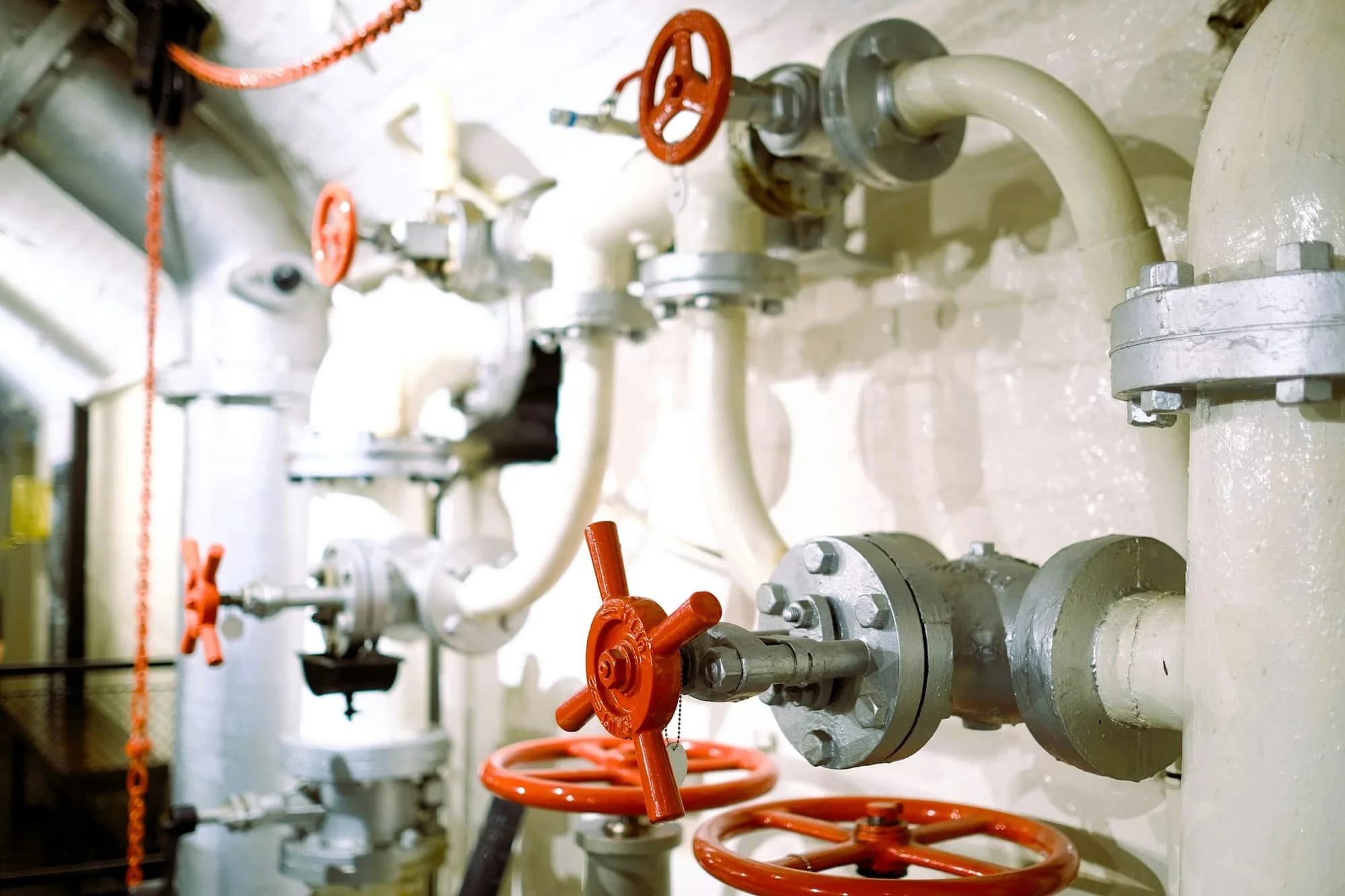 Cañerías industriales blancas con válvulas de volante rojas y manómetros en una sala de máquinas