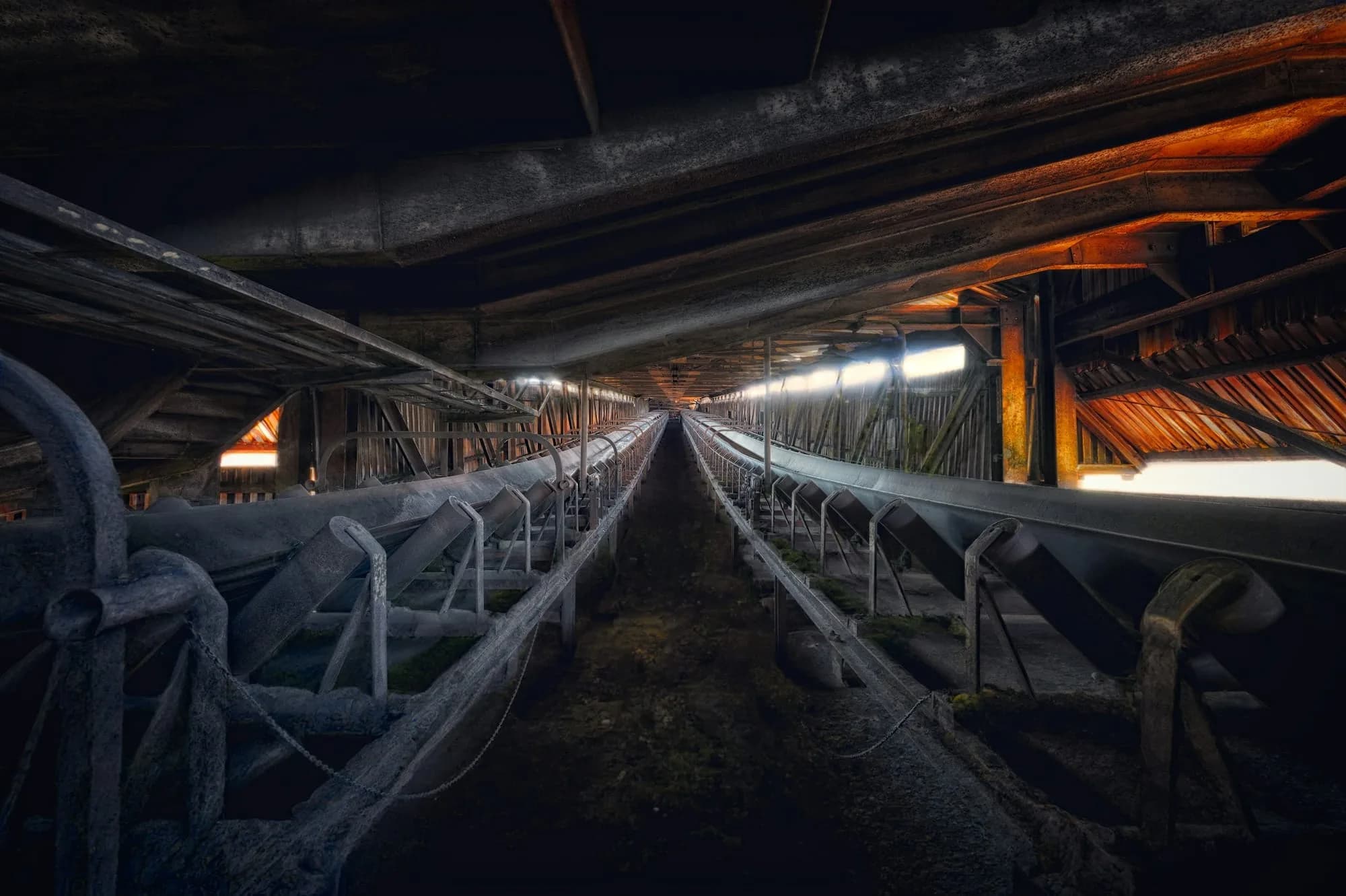 Larga cinta transportadora bajo la estructura de acero de una planta, vista en perspectiva con luz tenue